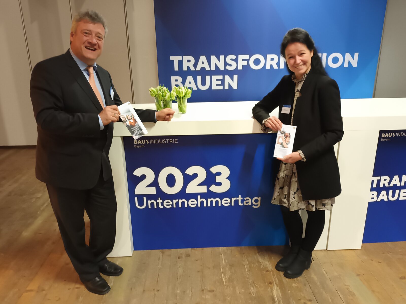 Günter Schmid und Sabine Tragl vor dem Plakat des Unternehmertages der Bauwirtschaft. Motto: Transformation Bauen